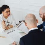Three business professionals in discussion over a contract in a modern office setting.