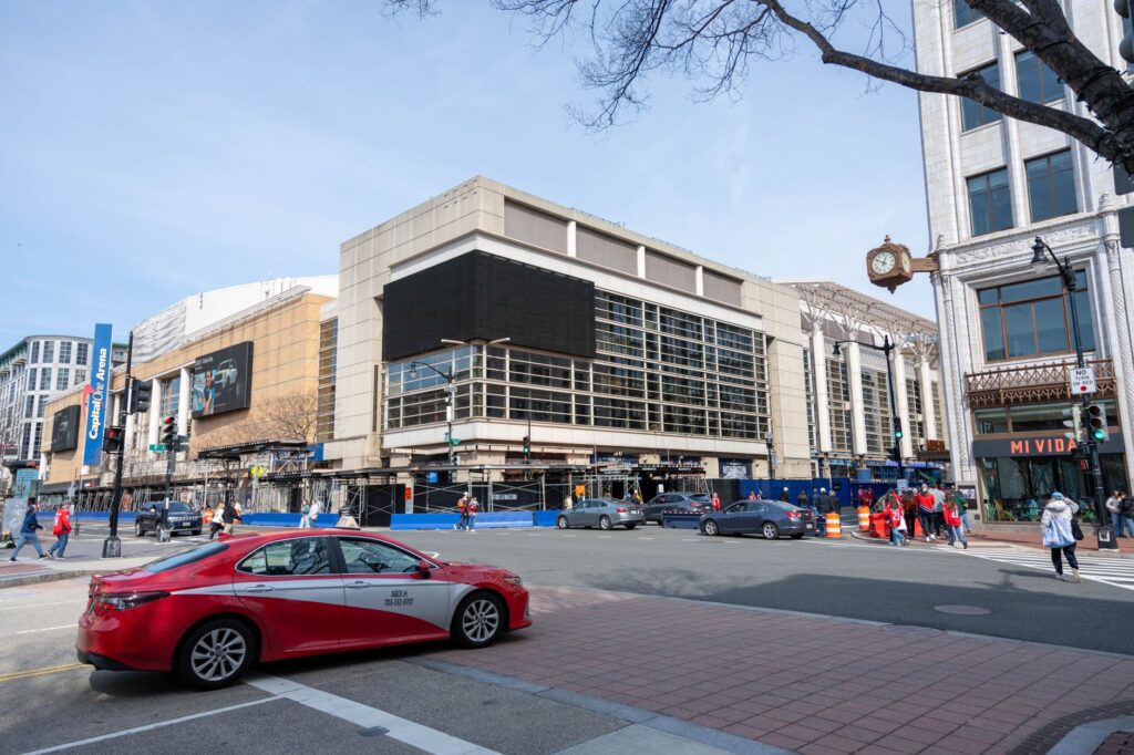 Cityscape featuring Capital One Arena in Washington D.C., bustling with people and traffic on a clear day.