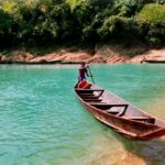 A person rowing a wooden boat on turquoise waters surrounded by lush greenery in Chattogram, Bangladesh.