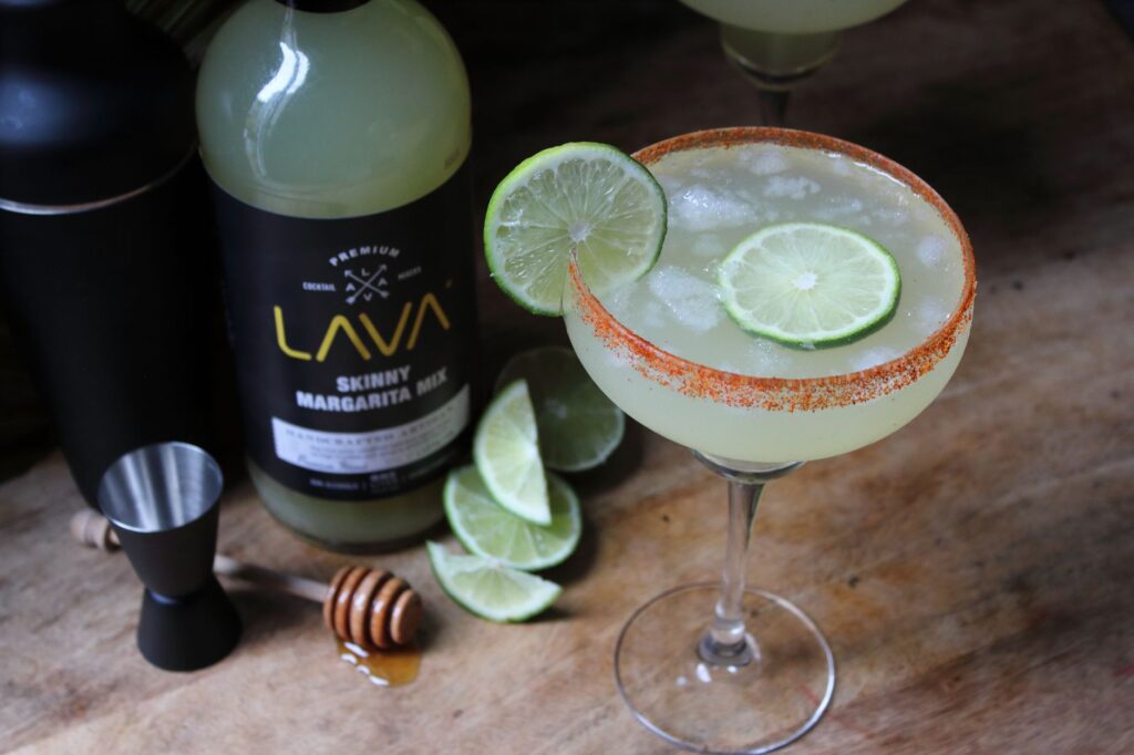 A vibrant margarita with fresh lime slices and mixer displayed on a wooden surface.
