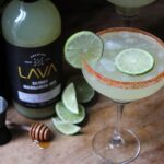 A vibrant margarita with fresh lime slices and mixer displayed on a wooden surface.