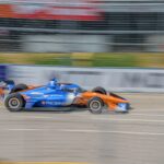 Orange and blue race car zooming on Toronto track, showcasing vibrant motion and racing dynamics.