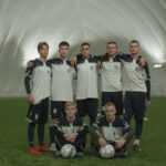 A group of young male soccer players in uniform posing on an indoor field.