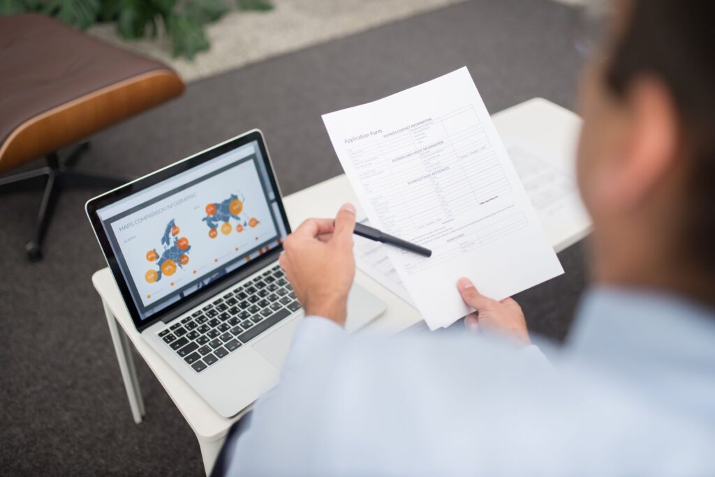Professional setting with businessman reviewing documents and data on a laptop in an office.