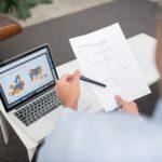 Professional setting with businessman reviewing documents and data on a laptop in an office.