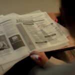 Person reviewing job listings in a newspaper, holding a pink marker for highlighting job ads.