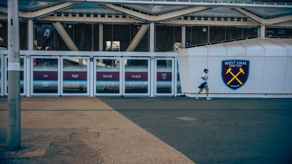 A person walking by West Ham United football stadium entrance in London.