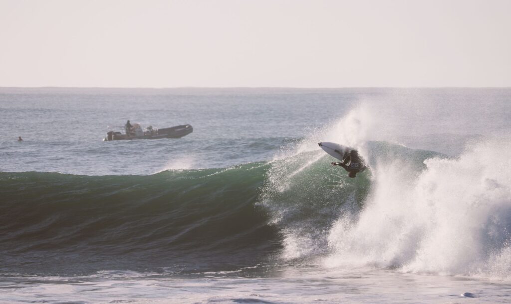 Surfer skillfully rides a powerful wave at Jeffreys Bay, South Africa, with support crew nearby.