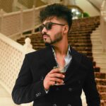 Fashionable man with sunglasses holding a drink at elegant indoor location.
