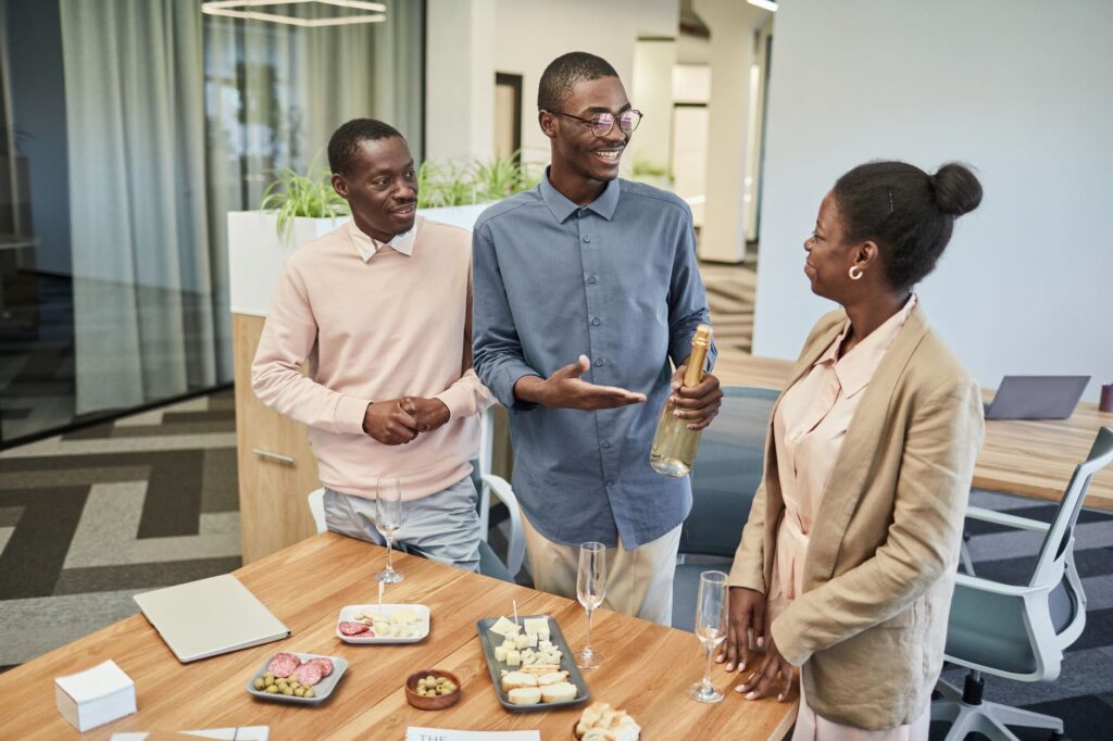 Colleagues celebrating with champagne and snacks in a modern office setting.