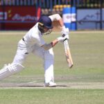 Action shot of a cricket player batting on the field during a sunny day match.