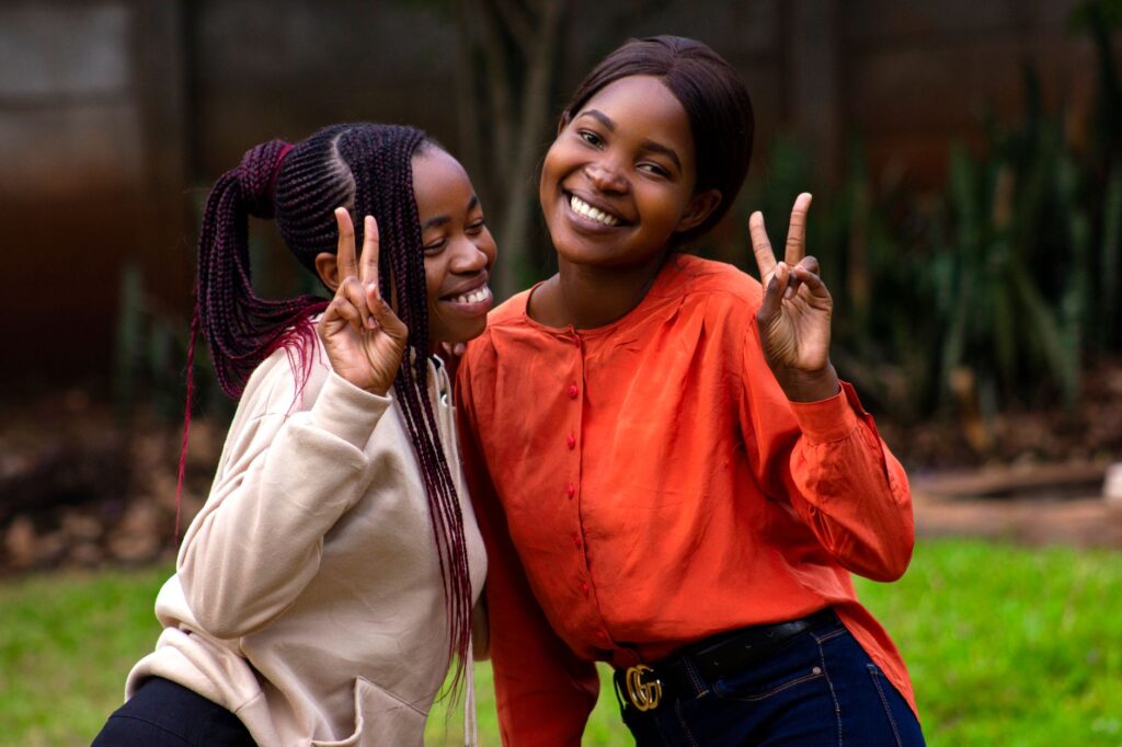 Two young women smiling and making peace signs outdoors in Harare, Zimbabwe.