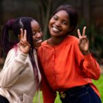 Two young women smiling and making peace signs outdoors in Harare, Zimbabwe.