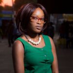 Portrait of a fashion-forward woman in a green dress and eyewear, captured on a city street at sunset.