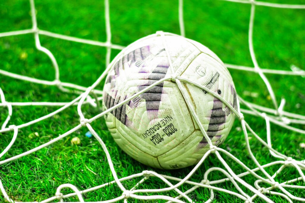 A close-up of a soccer ball caught in the net on a green grass field.