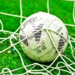 A close-up of a soccer ball caught in the net on a green grass field.