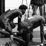 Black and white image of athletes in starting blocks ready for a sprint race indoors.