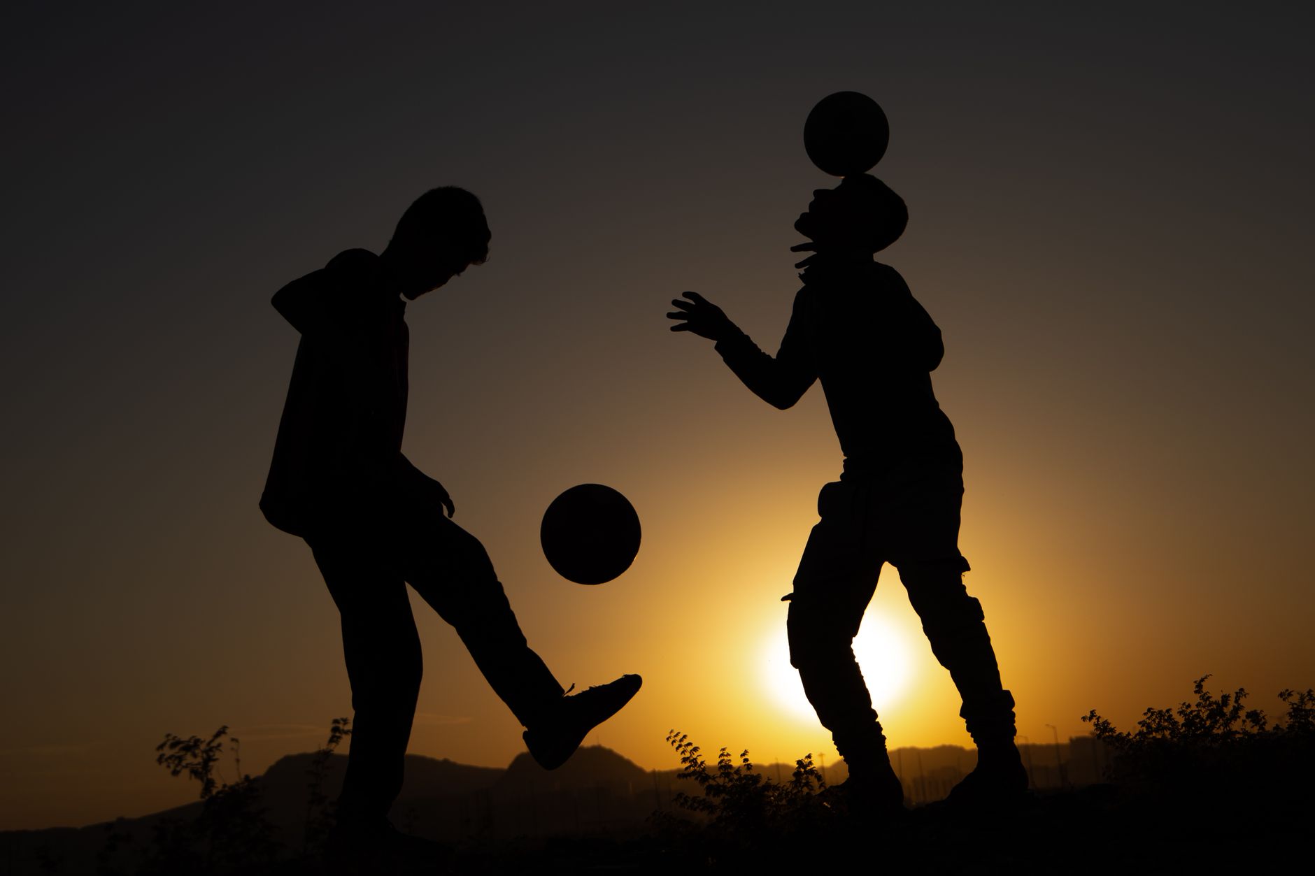 Silhouetted soccer players performing tricks at sunset, creating a scenic and dramatic view.