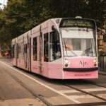 A vibrant pink tram travels down a tree-lined street in Melbourne, Australia.