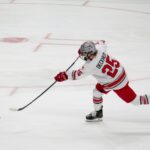 A professional ice hockey player takes a powerful shot on a rink.