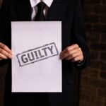 A businessman in a formal suit holding a sign with the word 'GUILTY.'