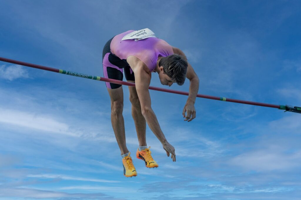 Dynamic capture of a pole vaulter clearing the bar under a clear blue sky.