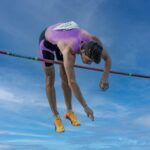 Dynamic capture of a pole vaulter clearing the bar under a clear blue sky.