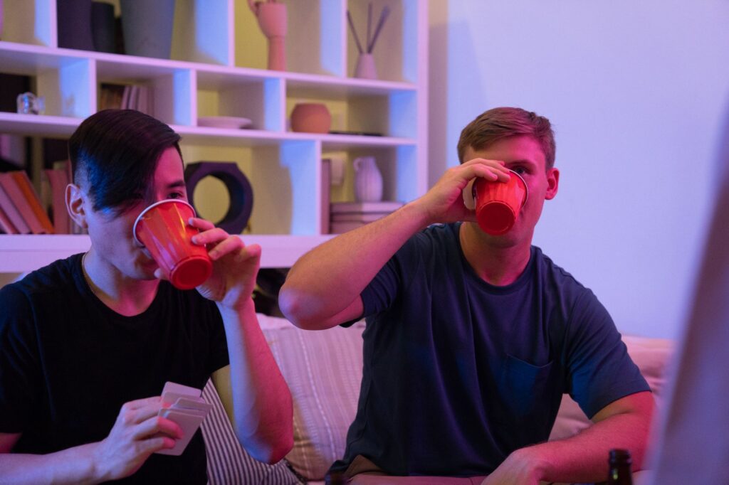 Two men having fun drinking and playing cards in a cozy indoor setting.