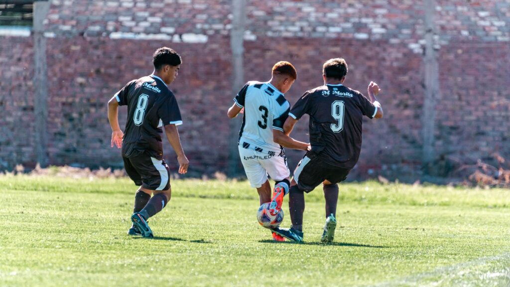 Capture of three soccer players competing for the ball during a match on a sunny day.