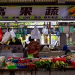 Bustling Asian market stall with vendor selling fresh produce and vegetables.