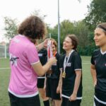 A women's football team receiving medals on the field, celebrating their victory.