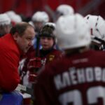 Male trainer talking with children in hockey uniform at ice rink during break of hockey game