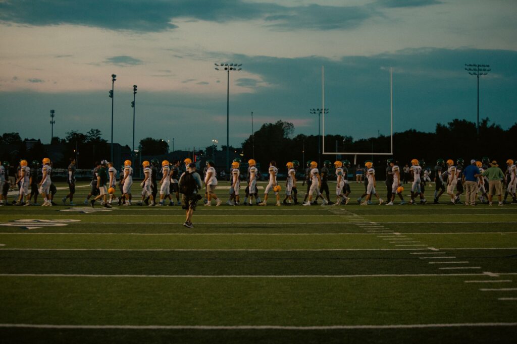 Players walking off football field at dusk after the game ends.