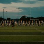 Players walking off football field at dusk after the game ends.