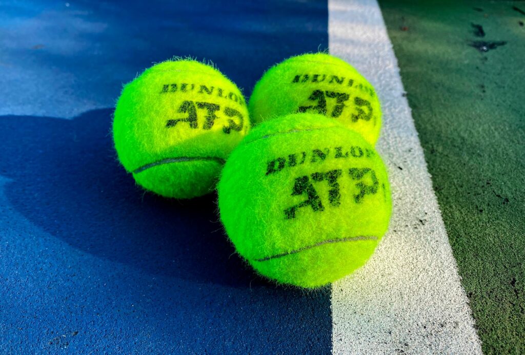 Vivid close-up of three Dunlop ATP tennis balls on a colorful outdoor court.