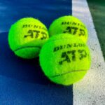 Vivid close-up of three Dunlop ATP tennis balls on a colorful outdoor court.