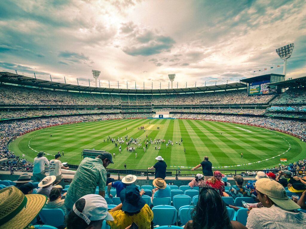 A lively cricket match at Melbourne Cricket Ground with a colorful crowd under a dynamic sky.