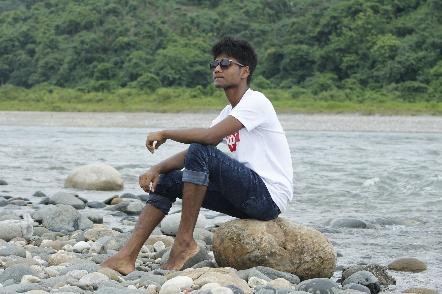 A young man sits on rocks by a river in Sylhet, Bangladesh.