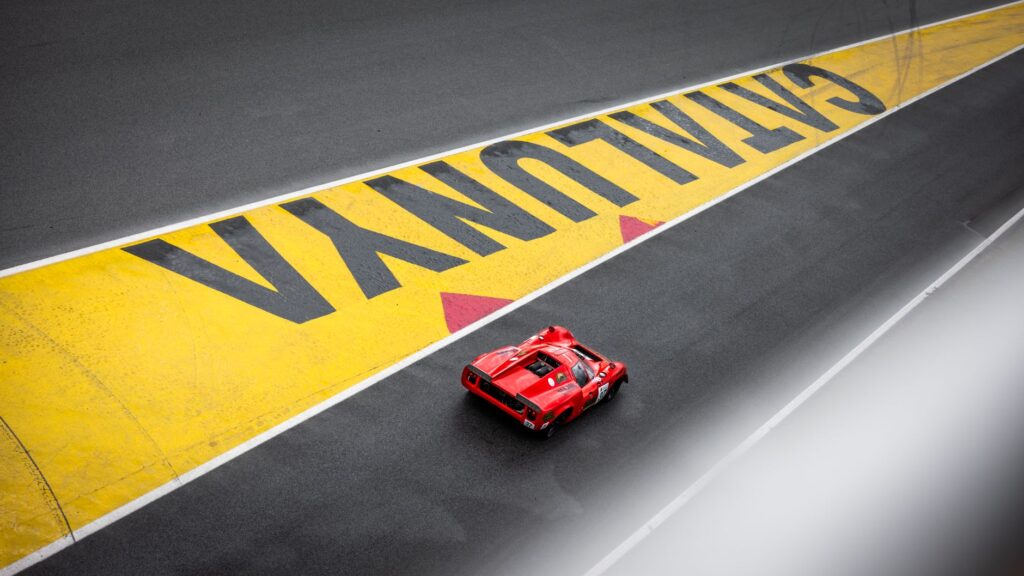 Red sports car racing on Circuit de Catalunya track, zoomed view.