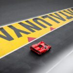 Red sports car racing on Circuit de Catalunya track, zoomed view.