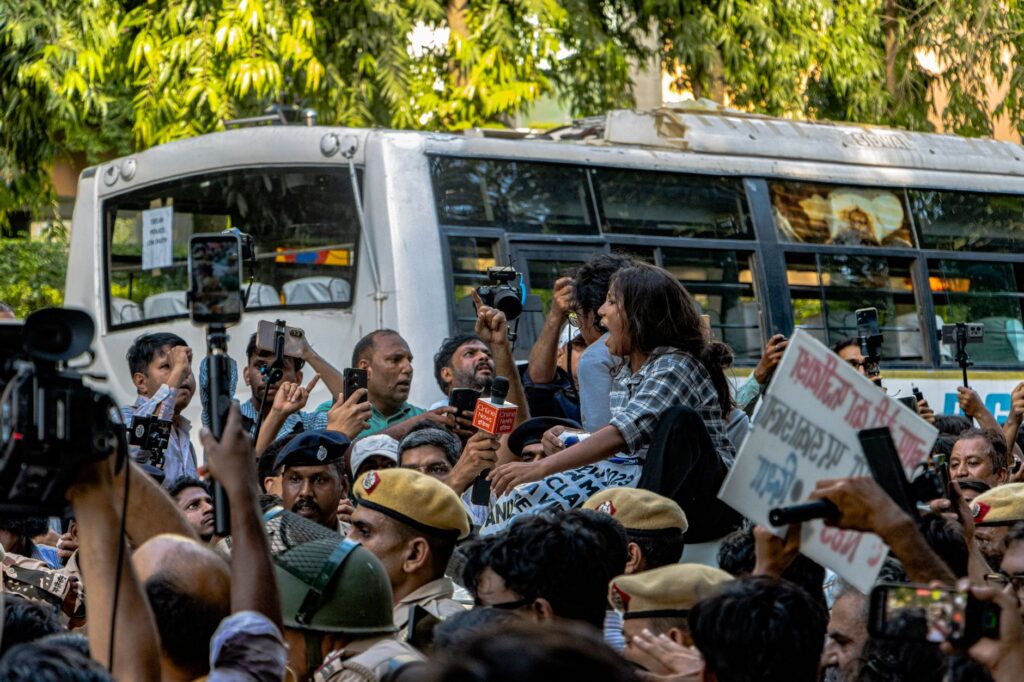 Dynamic scene of a peaceful protest in New Delhi depicting a diverse crowd, police presence, and media coverage.