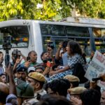 Dynamic scene of a peaceful protest in New Delhi depicting a diverse crowd, police presence, and media coverage.
