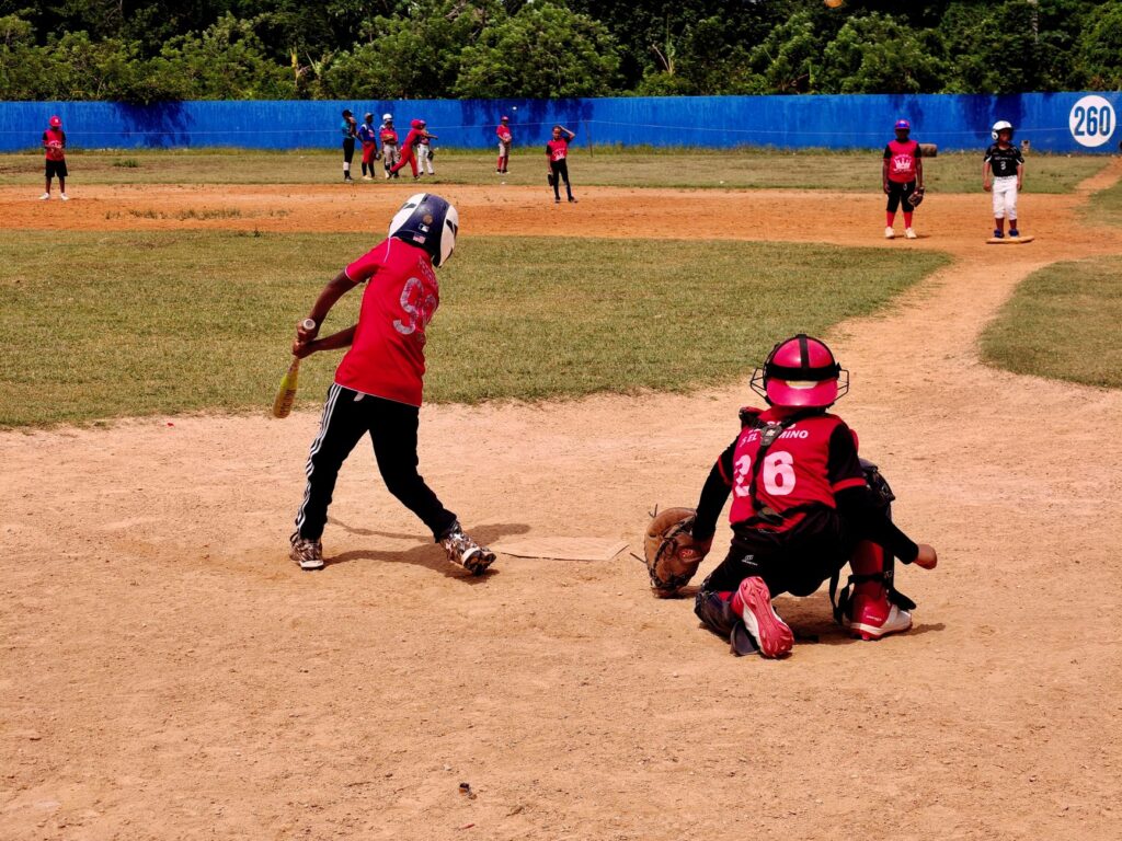 A youth baseball game in progress with kids playing on a sunny day, wearing protective gear.