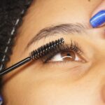 Detailed shot of eyelash extension application on a woman with blue painted nails.