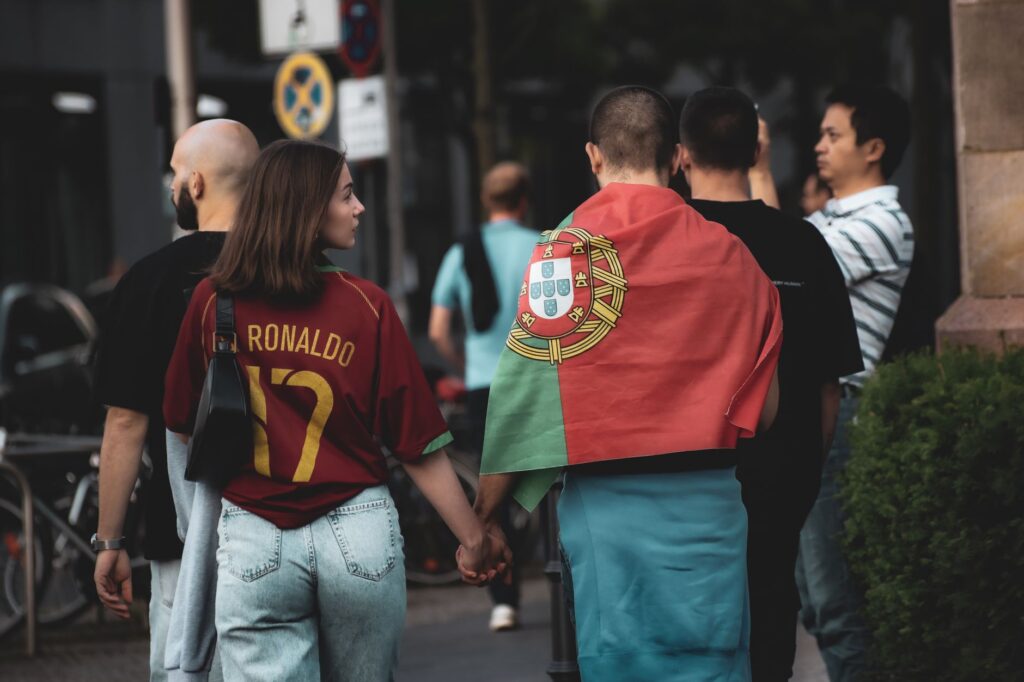 A group of football fans in Berlin, one wearing a Portugal flag, walking the street.