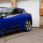 Blue electric vehicle charging at home using wall-mounted unit. Sustainable transportation solution.