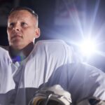 A focused ice hockey player in professional gear under stadium lights, ready for the game.