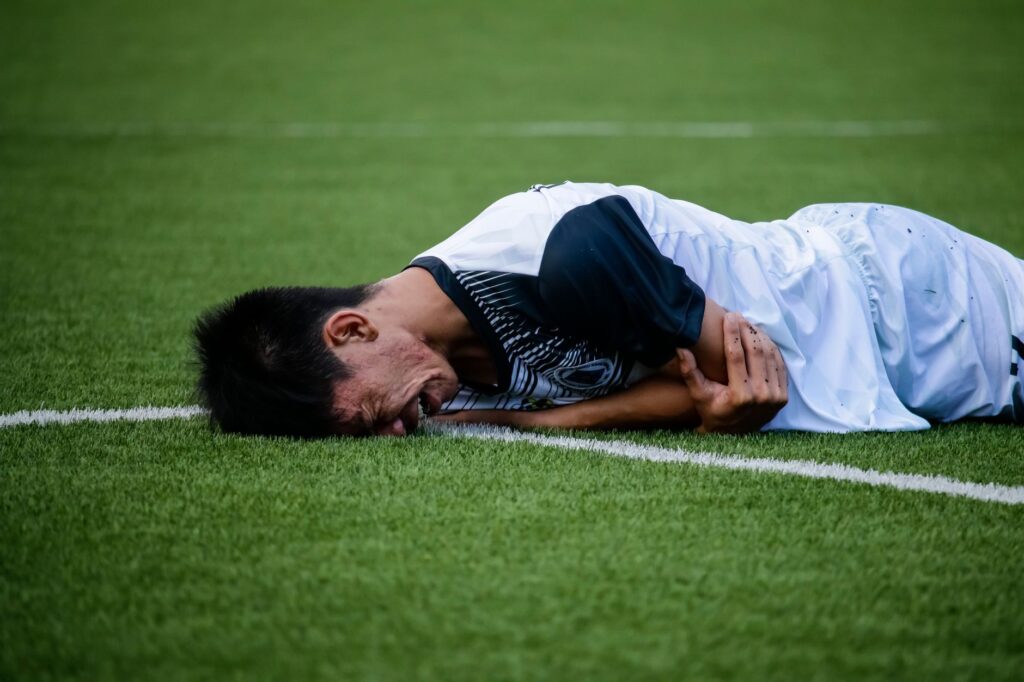 Soccer player lies on the field in pain during a game, indicating possible injury.