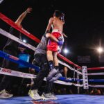 A boxer being lifted in celebration after a victory in the boxing ring, surrounded by trainers and spectators.