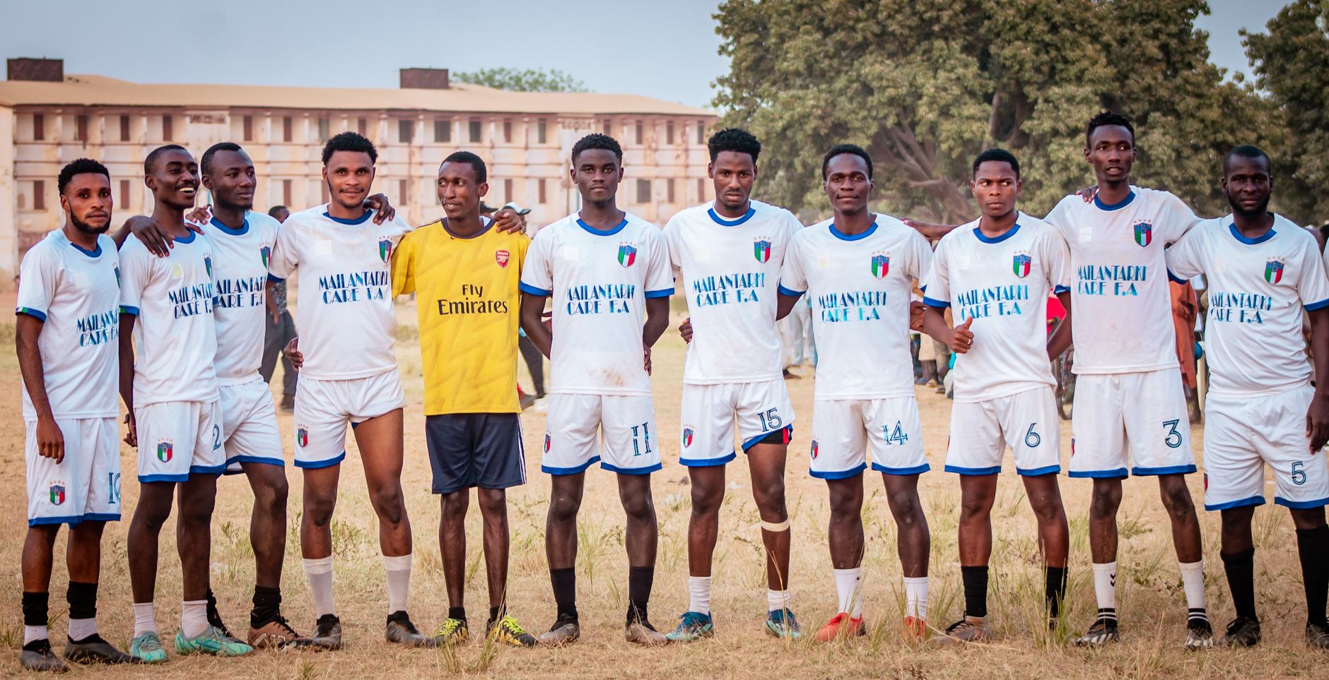 A local soccer team in uniforms posing on a grassy field under a clear sky.